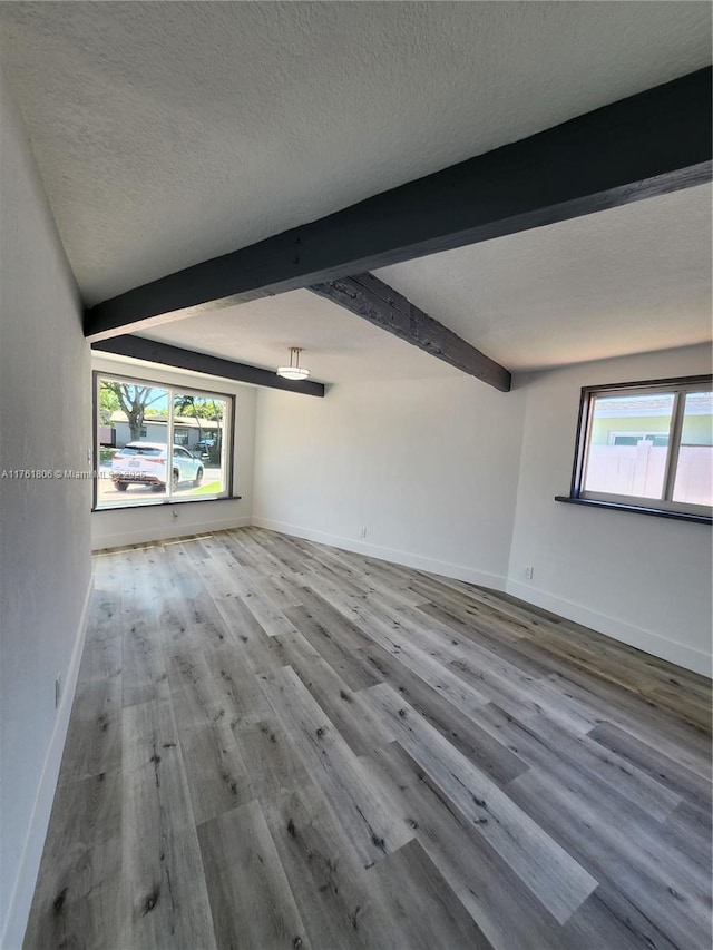 spare room featuring beamed ceiling, wood finished floors, baseboards, and a textured ceiling