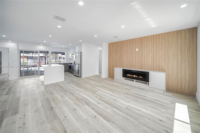 unfurnished living room with visible vents, wooden walls, a lit fireplace, and light wood finished floors