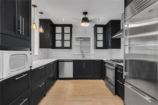 kitchen featuring backsplash, glass insert cabinets, light countertops, dark cabinetry, and stainless steel appliances