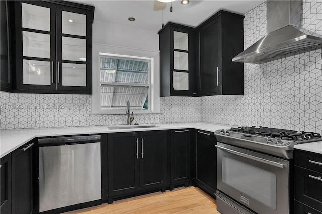 kitchen with wall chimney range hood, light countertops, appliances with stainless steel finishes, dark cabinetry, and a sink