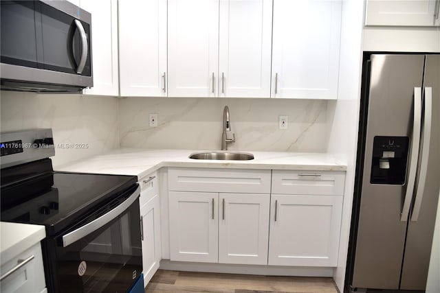 kitchen with backsplash, light stone countertops, stainless steel appliances, white cabinetry, and a sink