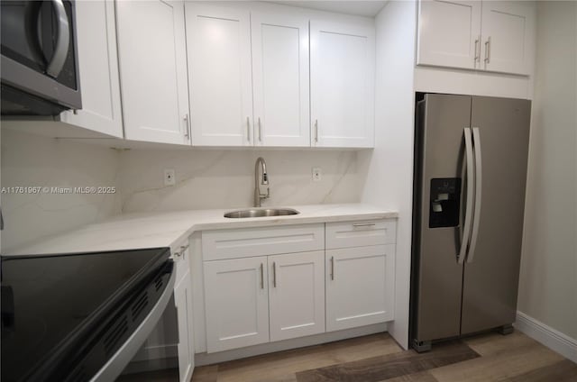 kitchen featuring white cabinetry, stainless steel appliances, light wood-style floors, and a sink