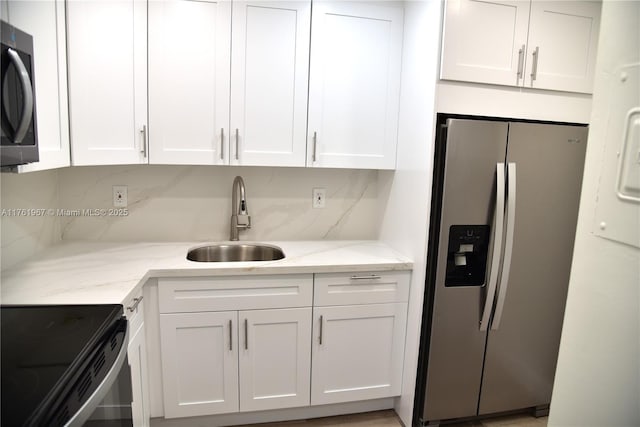 kitchen featuring light stone countertops, appliances with stainless steel finishes, white cabinetry, and a sink