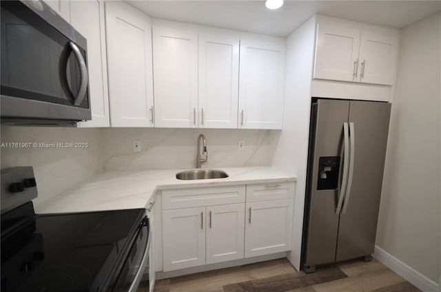 kitchen with baseboards, light wood-type flooring, white cabinets, stainless steel appliances, and a sink