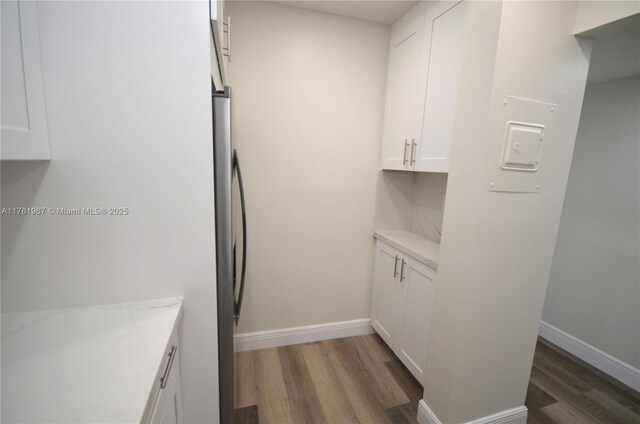 6070 W 18th Ave Unit 310, Hialeah, FL 33012 - kitchen featuring wood finished floors, white cabinetry, light stone countertops, baseboards, and freestanding refrigerator