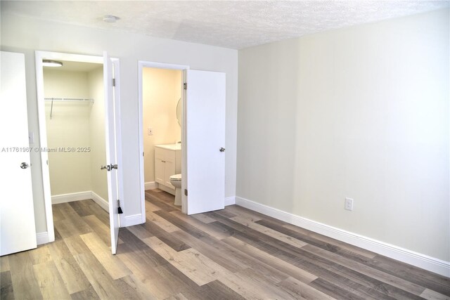 6070 W 18th Ave Unit 310, Hialeah, FL 33012 - unfurnished bedroom with wood finished floors, a walk in closet, a closet, baseboards, and a textured ceiling