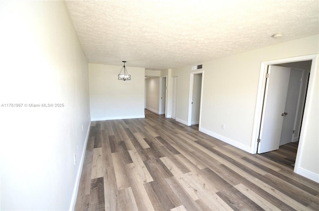 unfurnished room with baseboards, a textured ceiling, an inviting chandelier, and wood finished floors