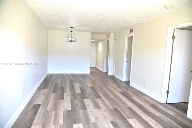 spare room with wood finished floors, baseboards, visible vents, a textured ceiling, and a notable chandelier