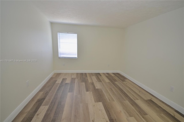 unfurnished room featuring baseboards, light wood finished floors, and a textured ceiling