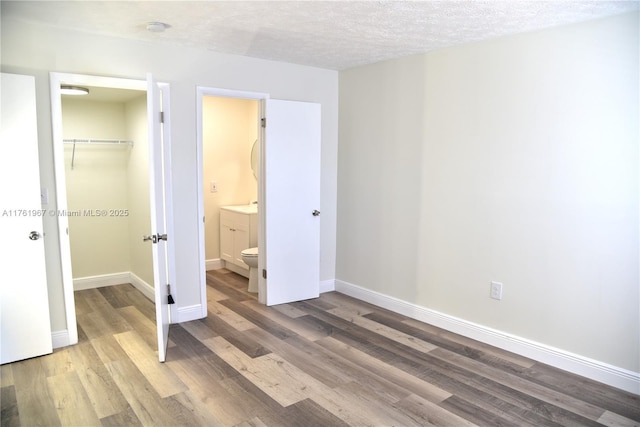 unfurnished bedroom with a textured ceiling, wood finished floors, a closet, baseboards, and a spacious closet