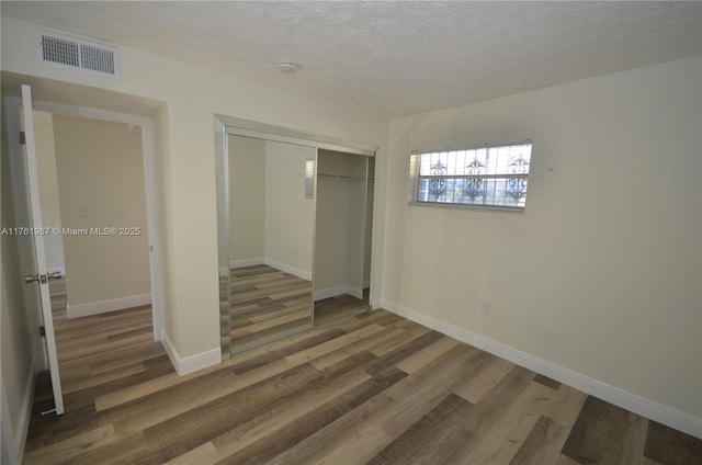 unfurnished bedroom with wood finished floors, baseboards, visible vents, a closet, and a textured ceiling