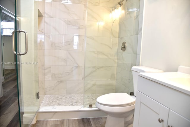 bathroom featuring vanity, toilet, wood finished floors, and a stall shower