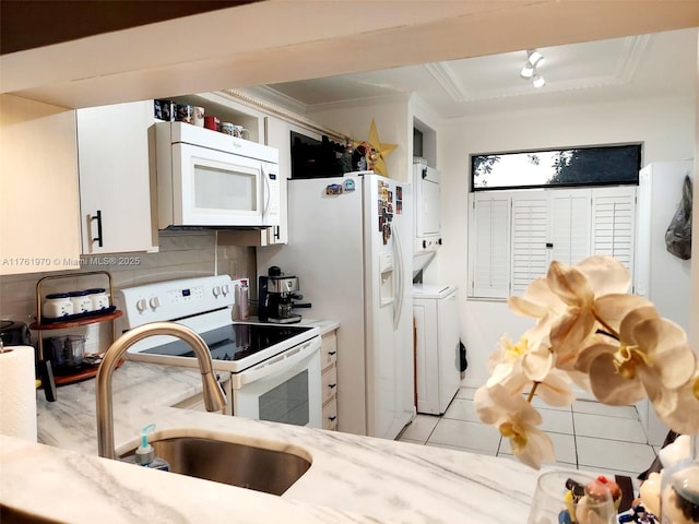 kitchen featuring white appliances, stacked washing maching and dryer, a sink, ornamental molding, and white cabinets