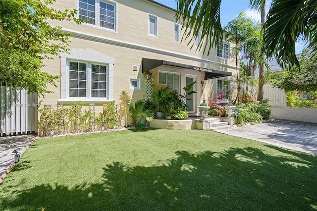 back of house featuring fence, a lawn, and stucco siding