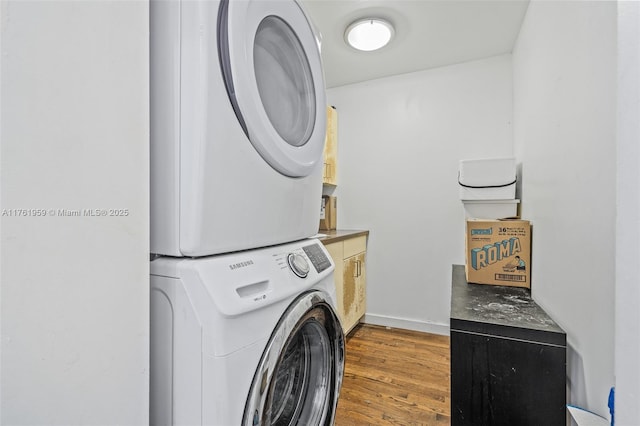 laundry room with wood finished floors, stacked washer / dryer, cabinet space, and baseboards