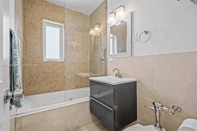 bathroom featuring tile patterned floors, tiled shower / bath, toilet, tile walls, and vanity