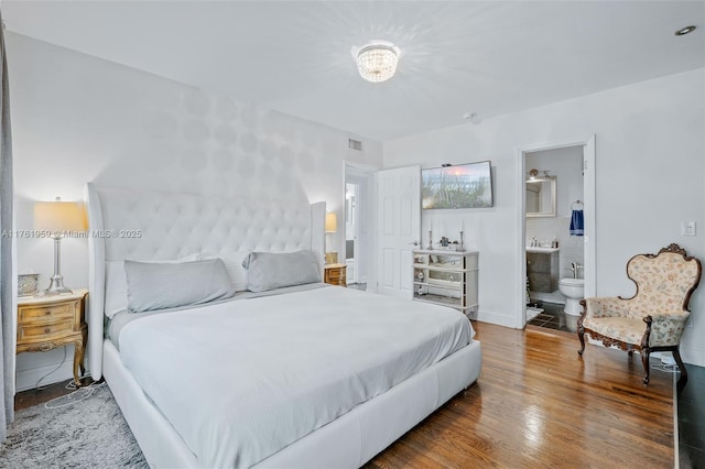 bedroom with visible vents, baseboards, ensuite bath, and wood finished floors