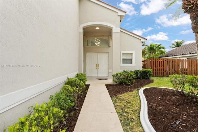 doorway to property featuring stucco siding and fence