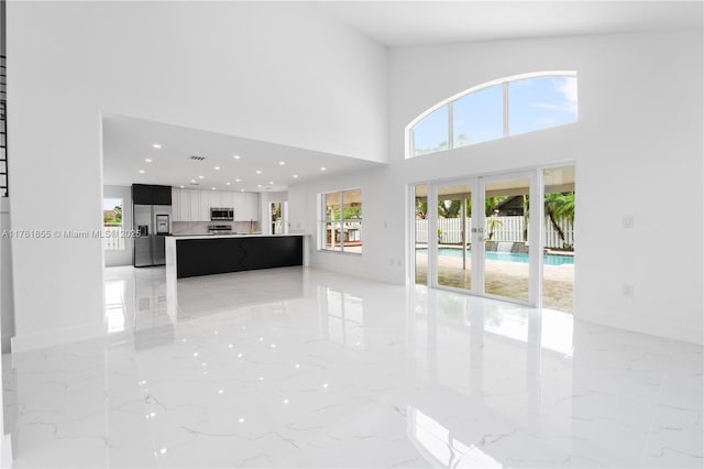 unfurnished living room featuring visible vents, marble finish floor, french doors, and a towering ceiling