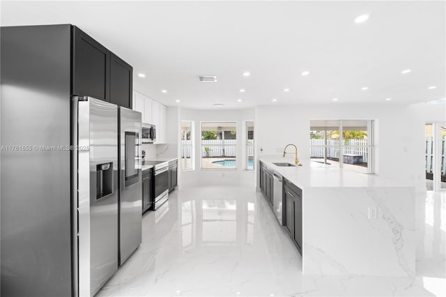 kitchen with marble finish floor, a sink, dark cabinetry, recessed lighting, and stainless steel appliances