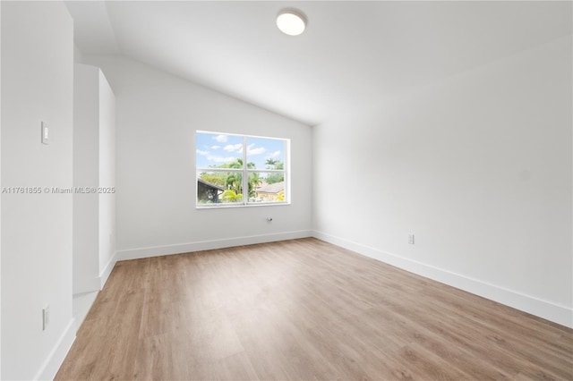 spare room with baseboards, lofted ceiling, and light wood-style flooring