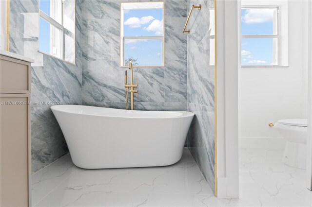 bathroom featuring a soaking tub, a healthy amount of sunlight, and marble finish floor