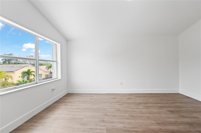 empty room featuring baseboards, light wood-style floors, and lofted ceiling