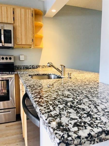 kitchen with stone counters, light wood finished floors, light brown cabinetry, a sink, and appliances with stainless steel finishes