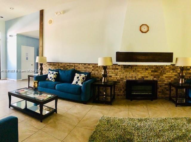 living area with tile patterned floors, a brick fireplace, and a high ceiling