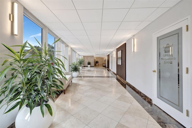 corridor featuring a paneled ceiling and baseboards