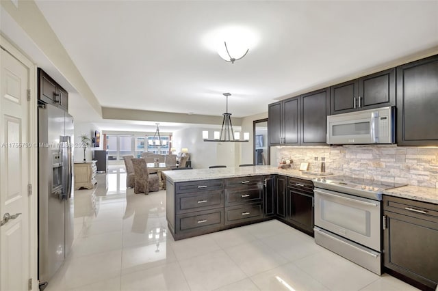 kitchen featuring a notable chandelier, light stone counters, backsplash, appliances with stainless steel finishes, and a peninsula