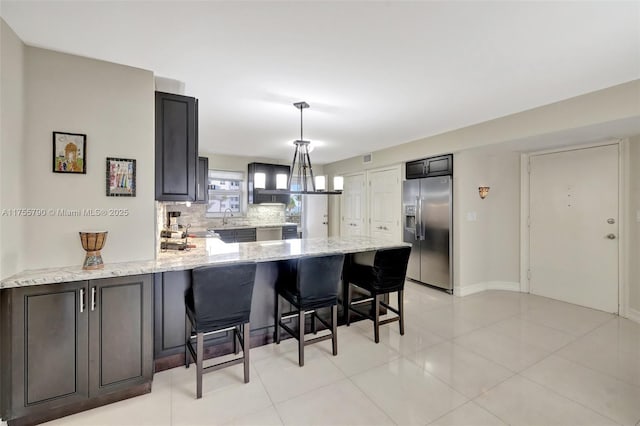 kitchen with light stone countertops, a kitchen bar, decorative backsplash, a peninsula, and stainless steel fridge