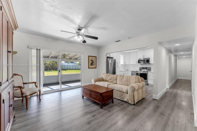 living area featuring visible vents, wood finished floors, baseboards, and ceiling fan