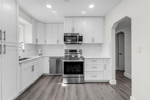 kitchen with light countertops, stainless steel appliances, light wood-style floors, white cabinetry, and a sink