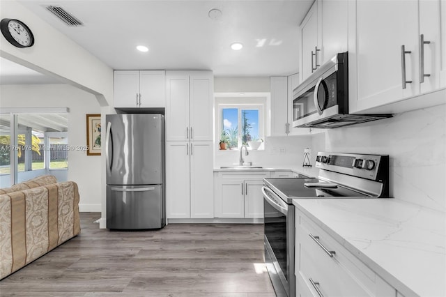 kitchen featuring visible vents, a sink, white cabinets, light wood-style floors, and appliances with stainless steel finishes