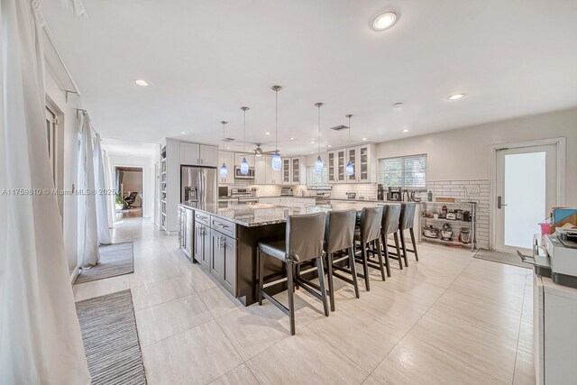 13700 SW 74th Ct, Palmetto Bay, FL 33158 - kitchen with stainless steel appliances, a spacious island, glass insert cabinets, light stone countertops, and backsplash