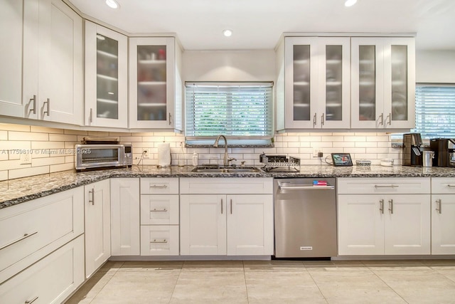 kitchen with dark stone countertops, a toaster, backsplash, and a sink