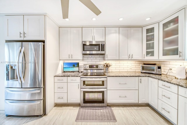 kitchen featuring backsplash, stainless steel appliances, a toaster, glass insert cabinets, and light stone countertops