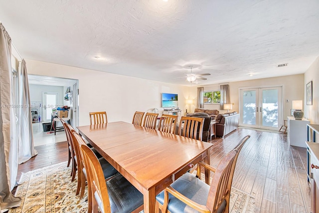 dining room with light wood finished floors, visible vents, ceiling fan, french doors, and a textured ceiling