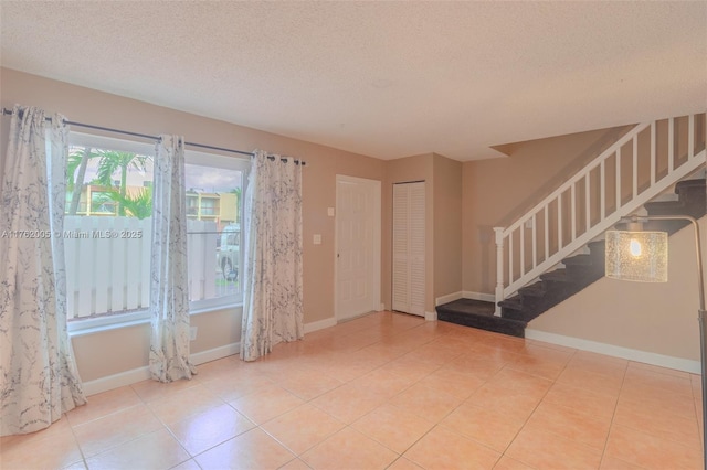 empty room featuring tile patterned floors, a textured ceiling, stairs, and baseboards