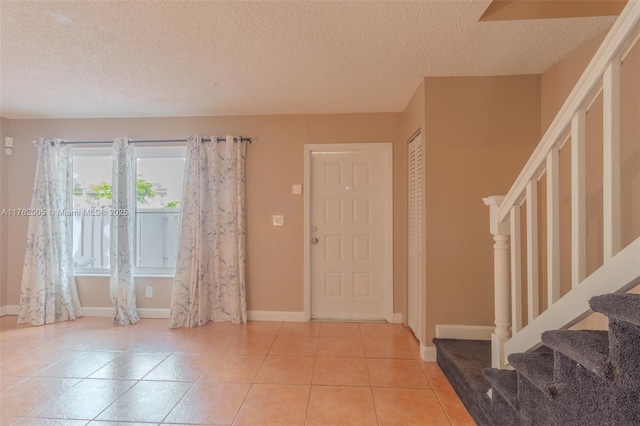 tiled entrance foyer featuring baseboards, a textured ceiling, and stairs