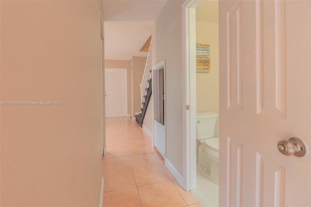 corridor with baseboards, light tile patterned flooring, and stairs