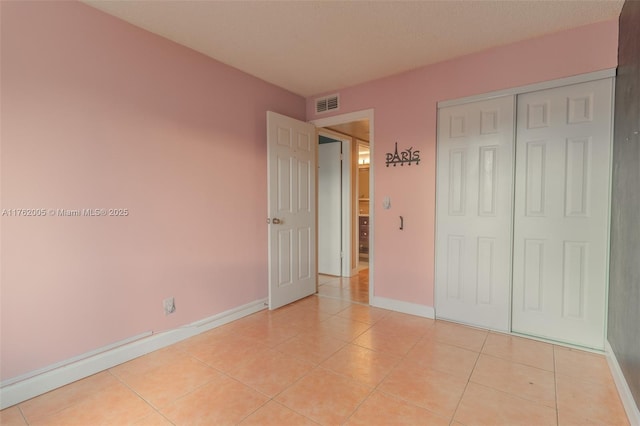 unfurnished bedroom featuring light tile patterned floors, visible vents, baseboards, and a closet