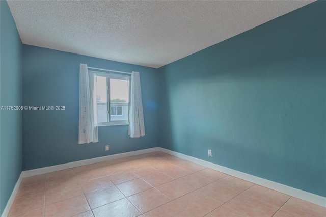 spare room featuring light tile patterned floors, baseboards, and a textured ceiling