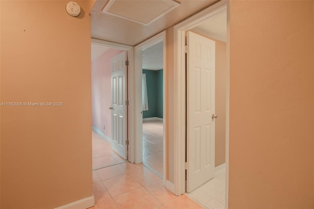 corridor featuring visible vents, baseboards, and light tile patterned flooring