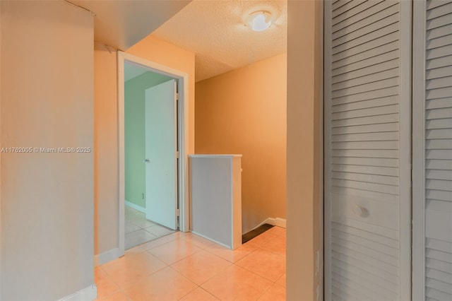 hallway featuring light tile patterned flooring, an upstairs landing, a textured ceiling, and baseboards