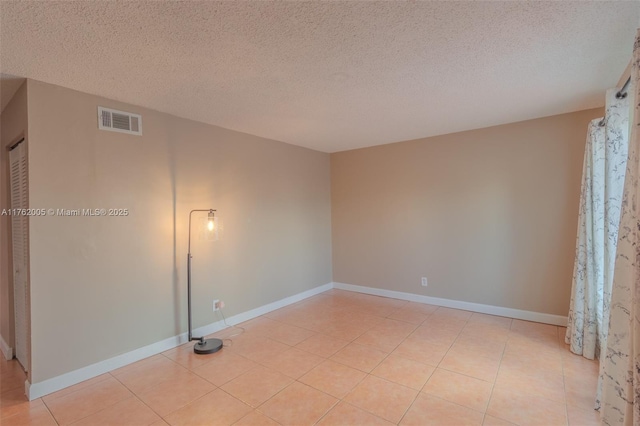 empty room featuring light tile patterned flooring, baseboards, visible vents, and a textured ceiling