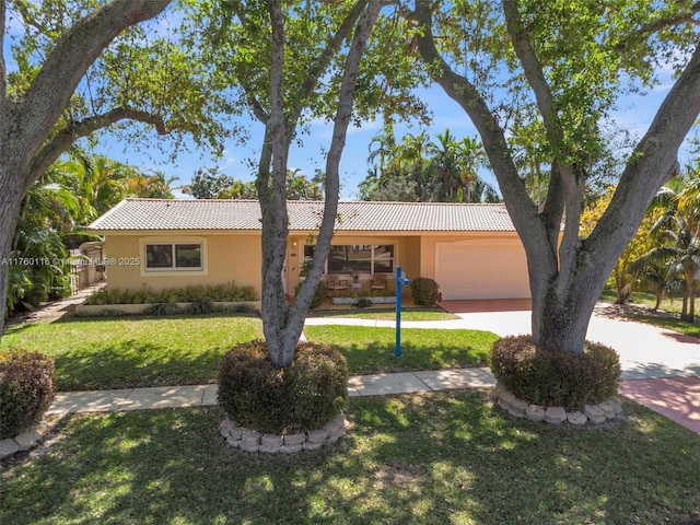 ranch-style home with a tile roof, concrete driveway, a front yard, stucco siding, and an attached garage