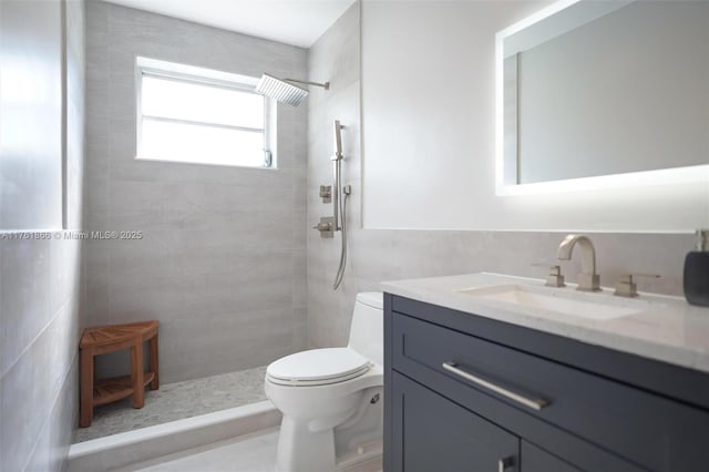 bathroom featuring vanity, tile walls, toilet, and a tile shower