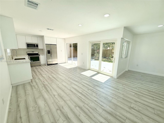 unfurnished living room with baseboards, visible vents, light wood-style flooring, recessed lighting, and a sink